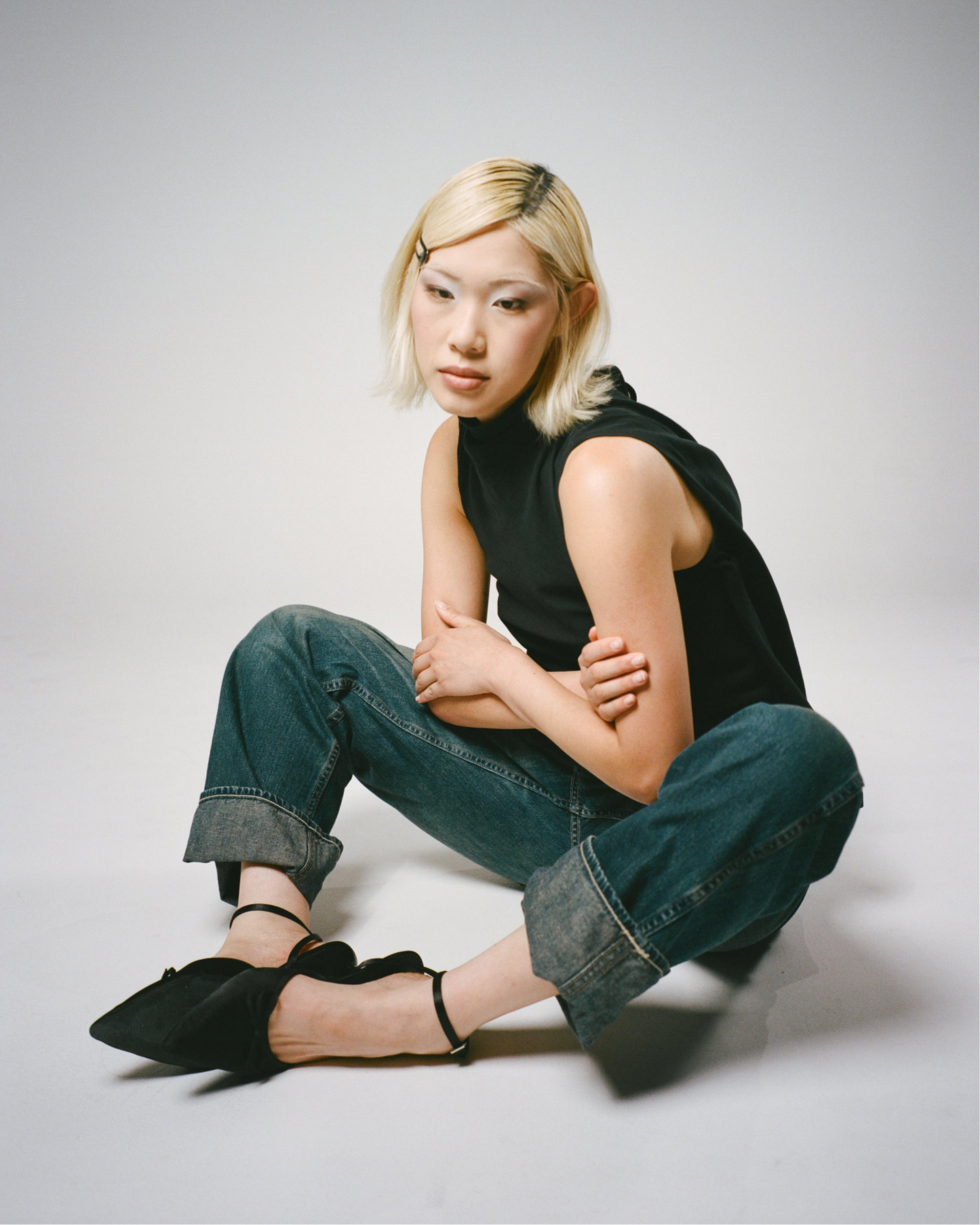 Person wearing a black sleeveless top and blue jeans sitting on a white background