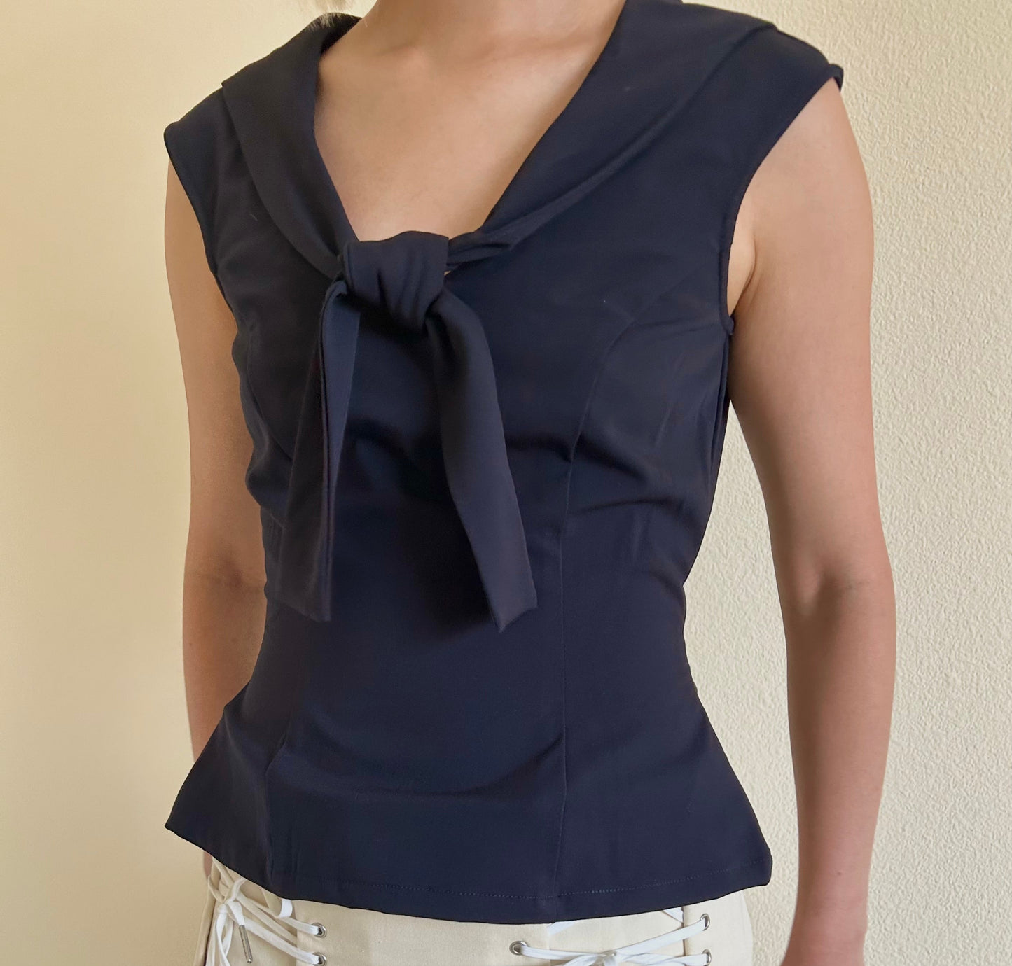 Navy sleeveless top with a bow detail worn by a person against a beige background