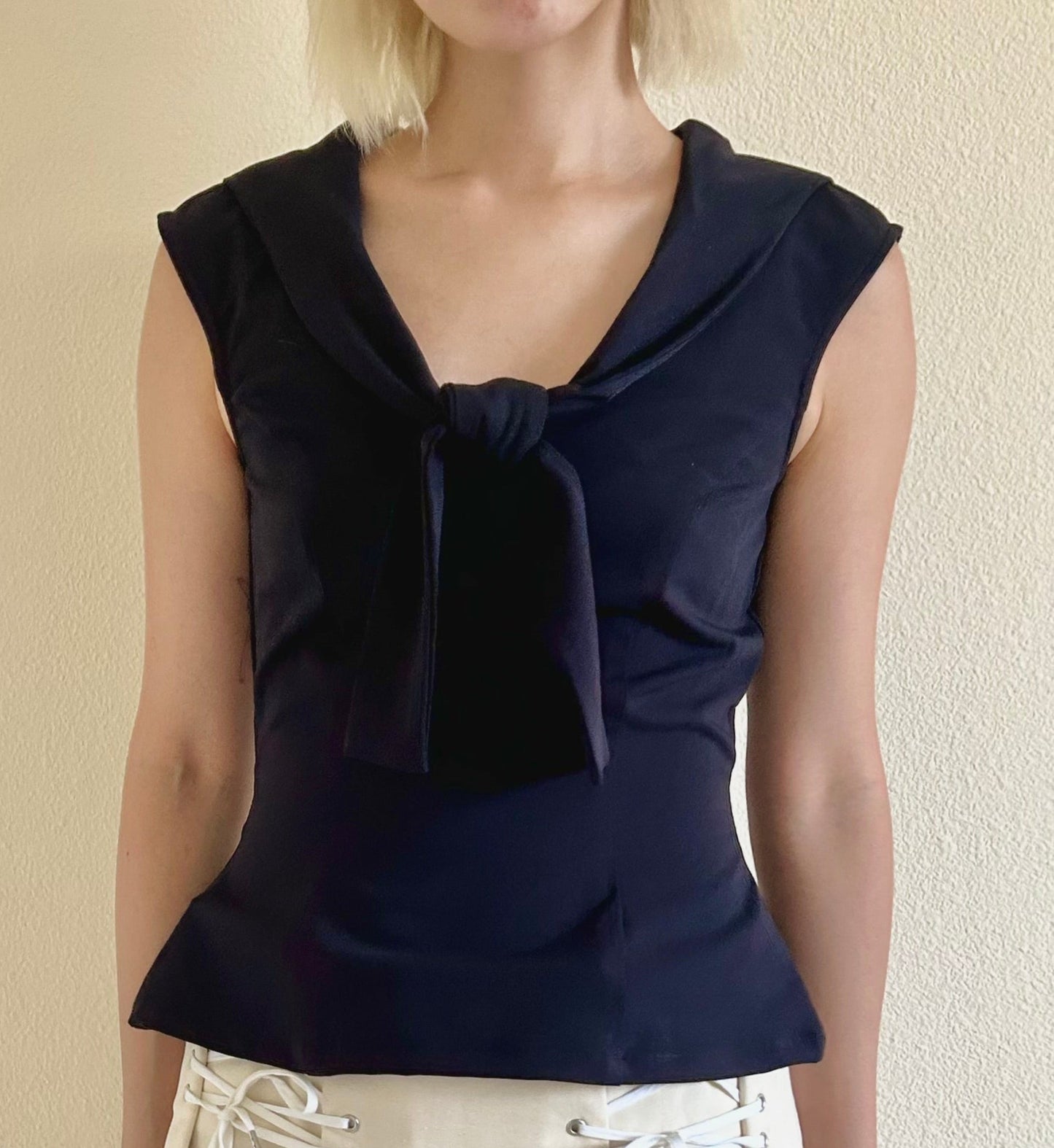 Woman wearing a navy blue top with a bow detail and a beige skirt against a plain background
