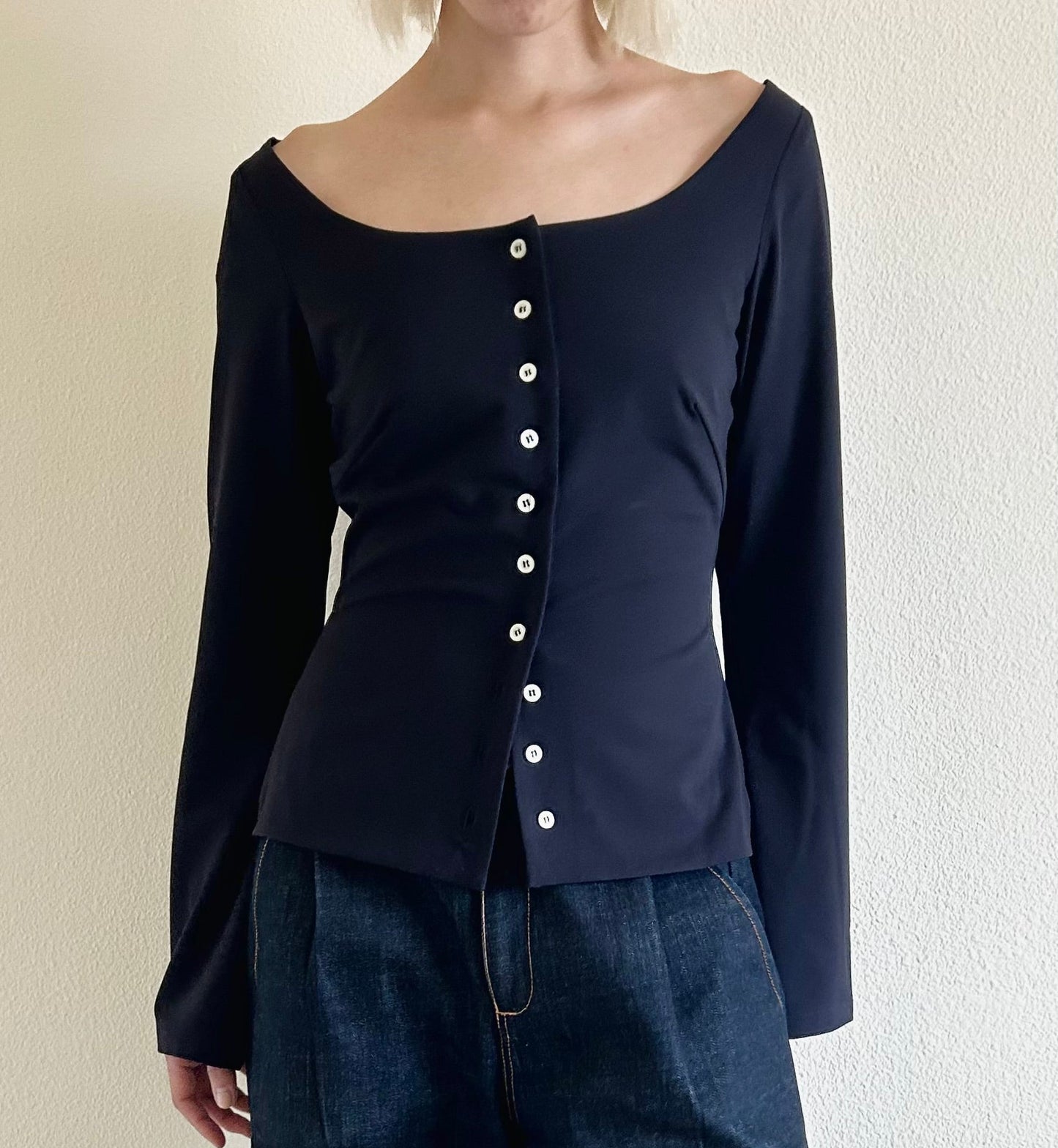 Person wearing a dark blue long-sleeve top with button details against a neutral background