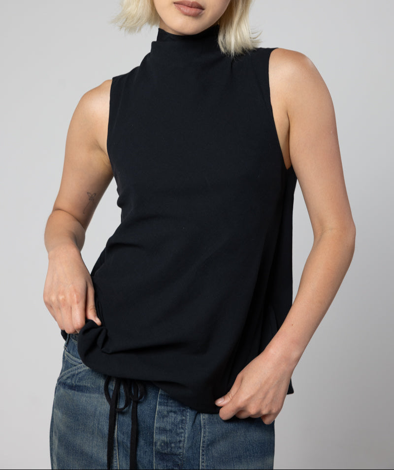 Person wearing a black sleeveless top and blue jeans against a gray background