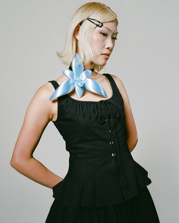 Woman wearing a black dress with a blue flower accessory on a gray background