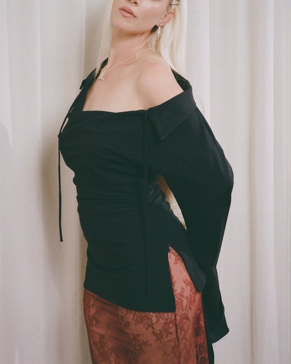Woman wearing a navy off-shoulder top and patterned pants against a white curtain background