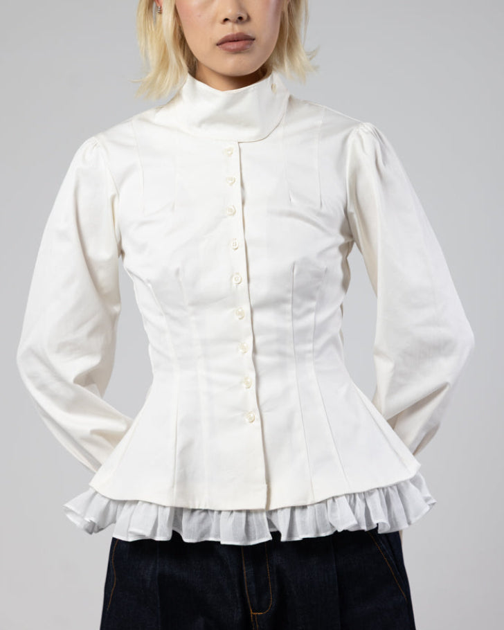 Person wearing a white blouse with ruffled details on a gray background